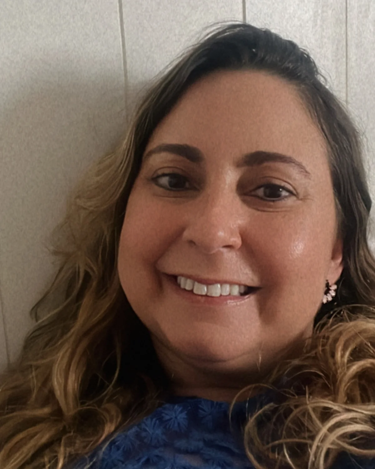 Dra. Aline Kárita sorrindo, de blusa azul, diante de uma parede clara